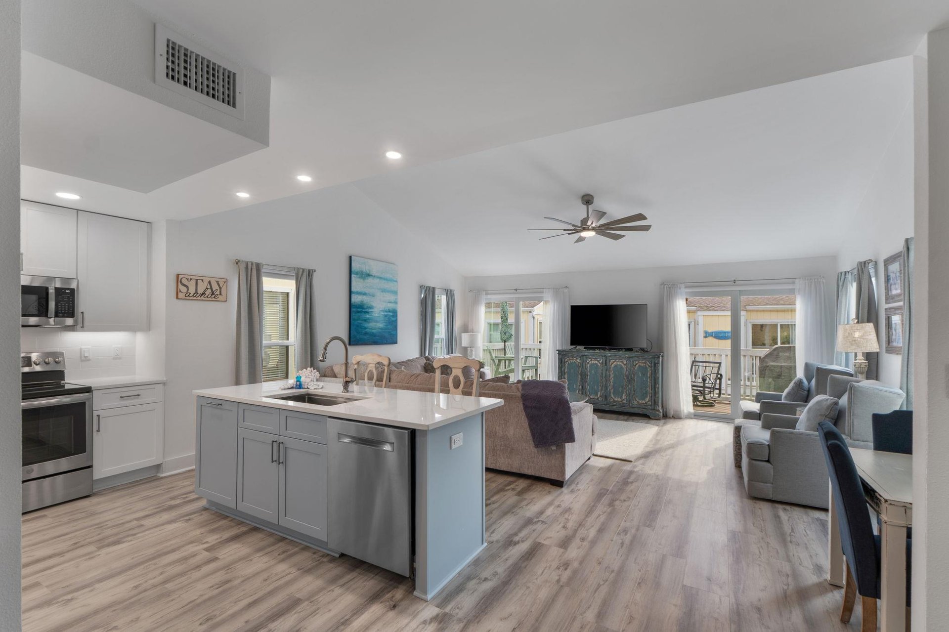 Relax in your openconcept living space with modern kitchen, comfy seating, and peaceful ocean artwork creating a coastal vibe.