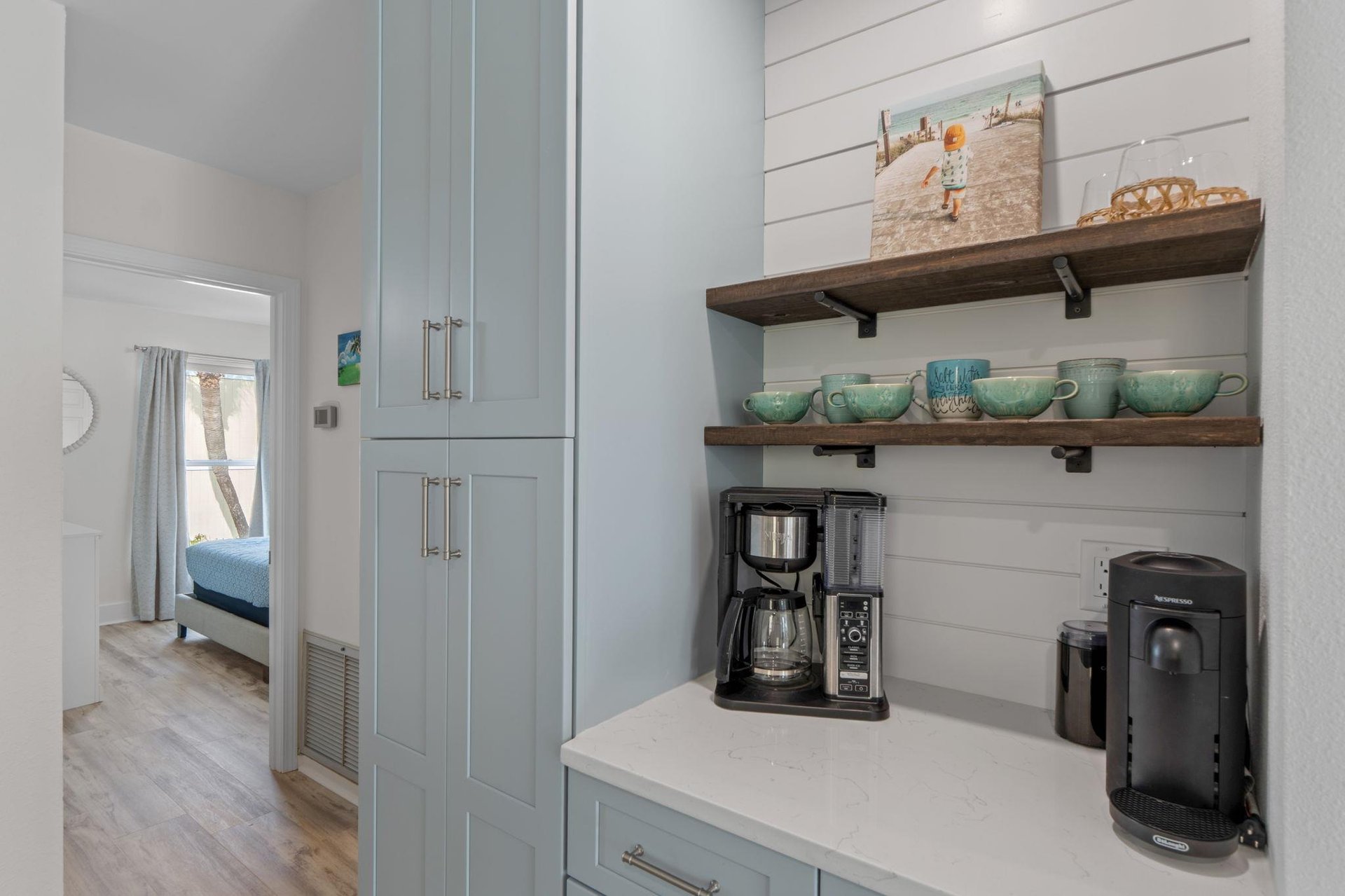 Your morning coffee ritual awaits in this charming kitchen nook, complete with premium coffee makers and elegant turquoise mugs on rustic wooden shelves.