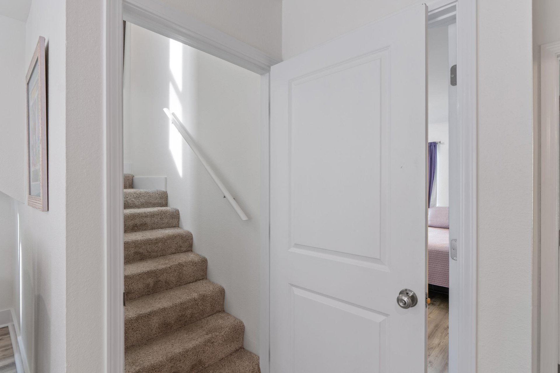 Bright hallway connects your spaces with carpeted stairs leading to upper level and glimpse into cozy bedroom.