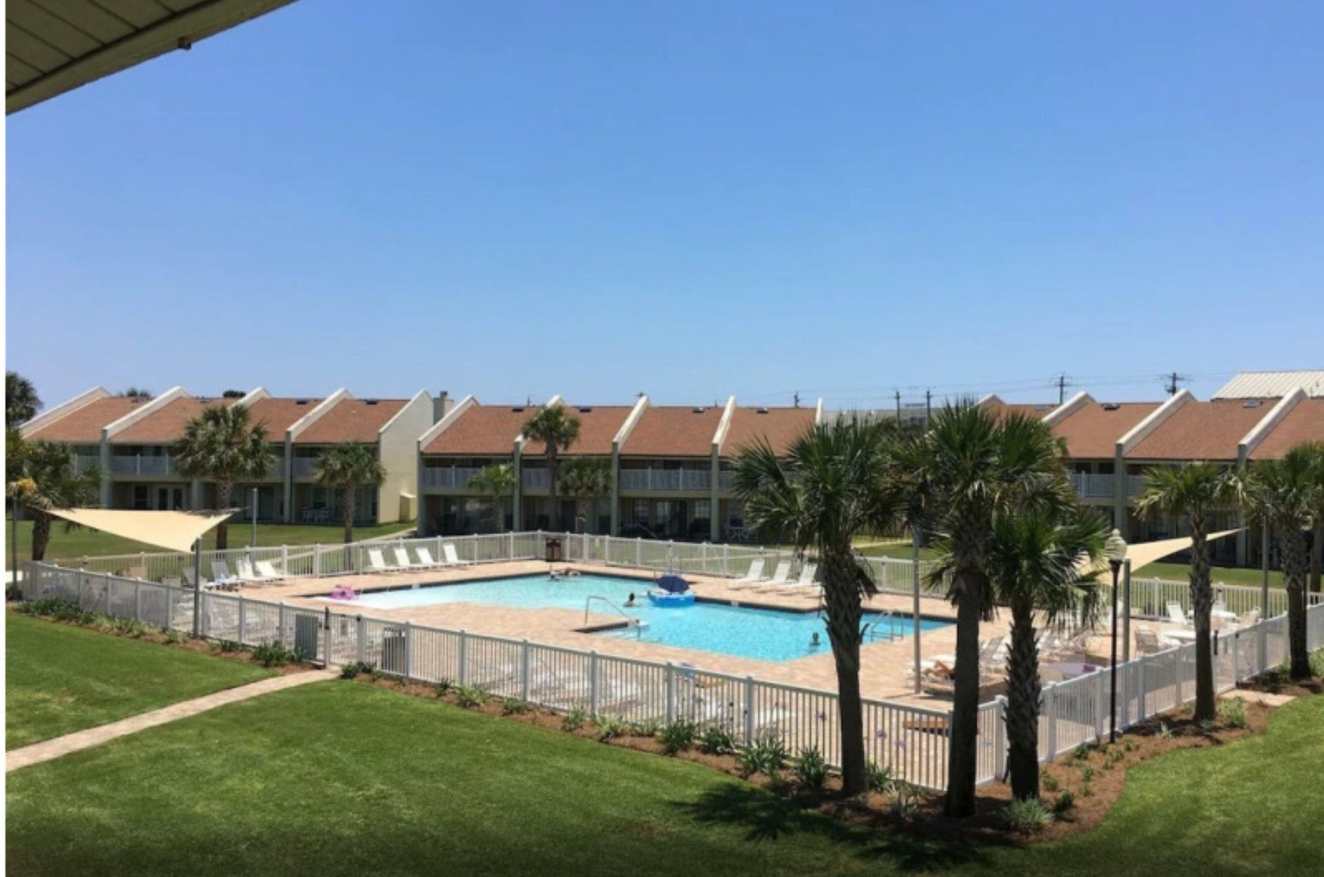 A gated community pool with a large sun deck and lots of loungers