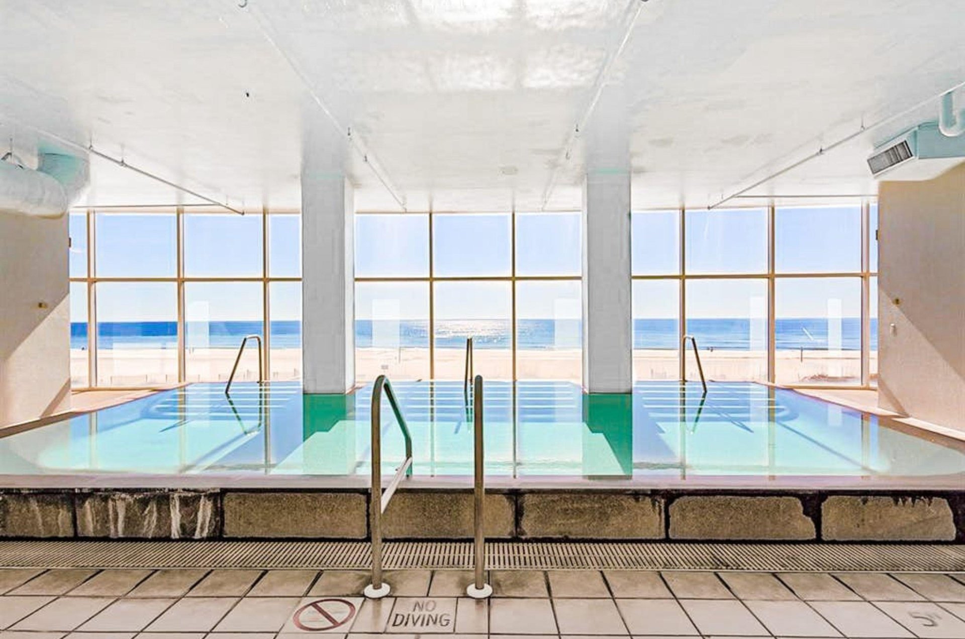 The indoor swimming pool next to floor to ceiling windows overlooking the beach at Island Tower