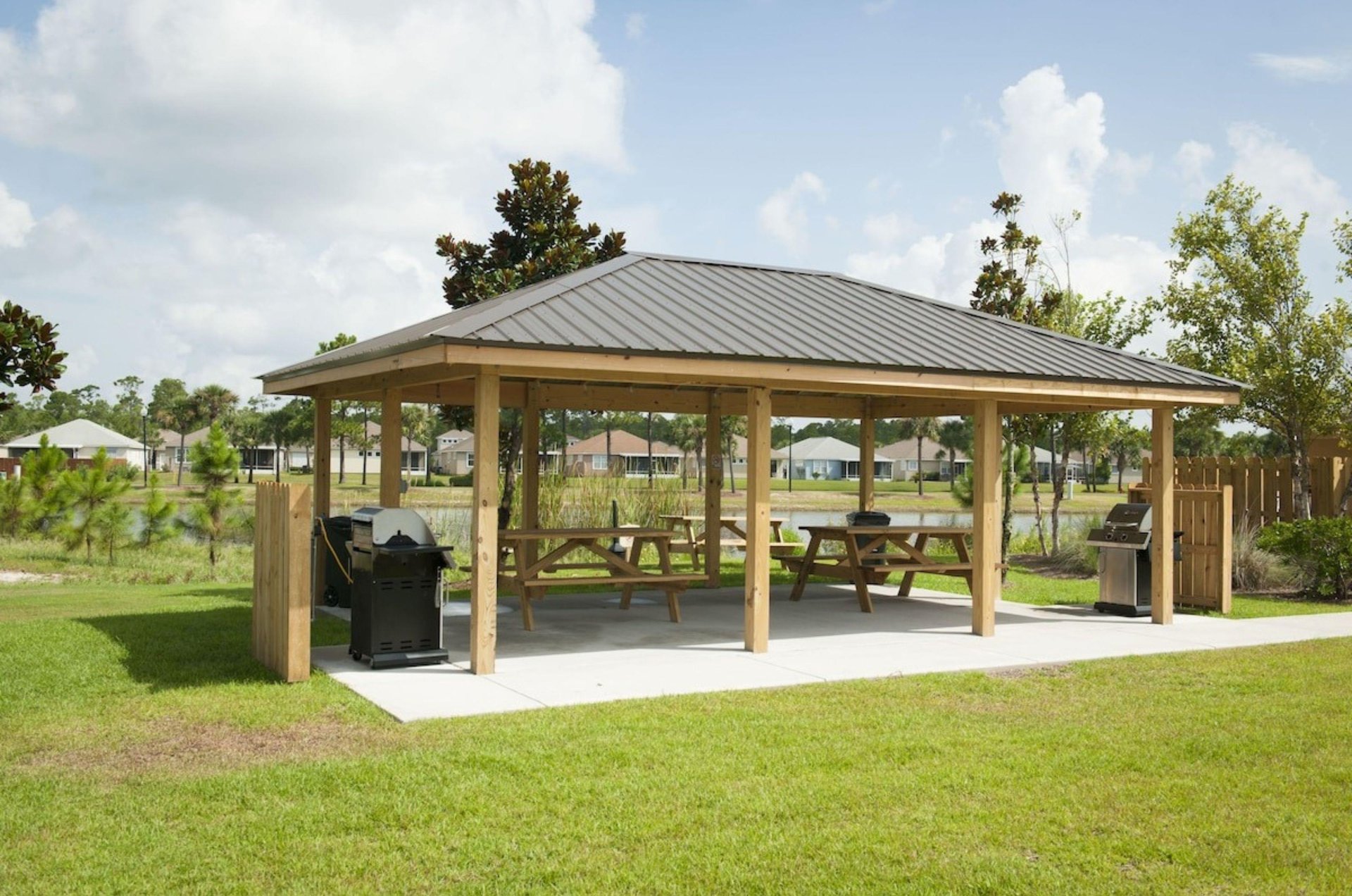 A covered outdoor patio with picnic tables nad barbecue grills
