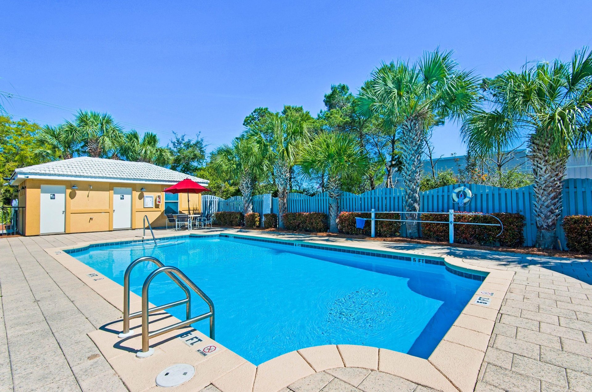 The complex swimming pool has nearby bathrooms and lush landscaping.