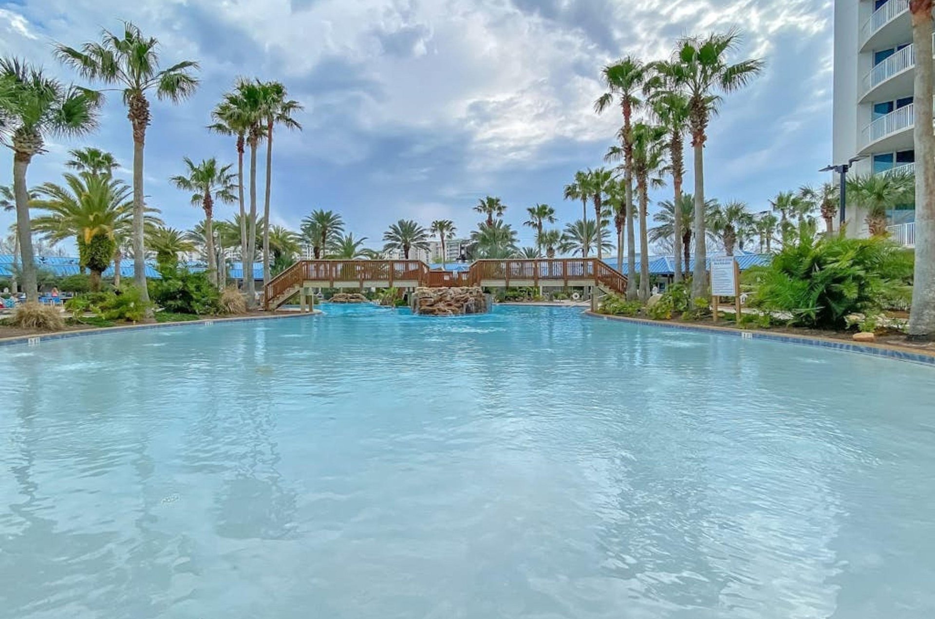 The large lagoonstyle pool at the Palms of Destin with a wooden bridge crossing over