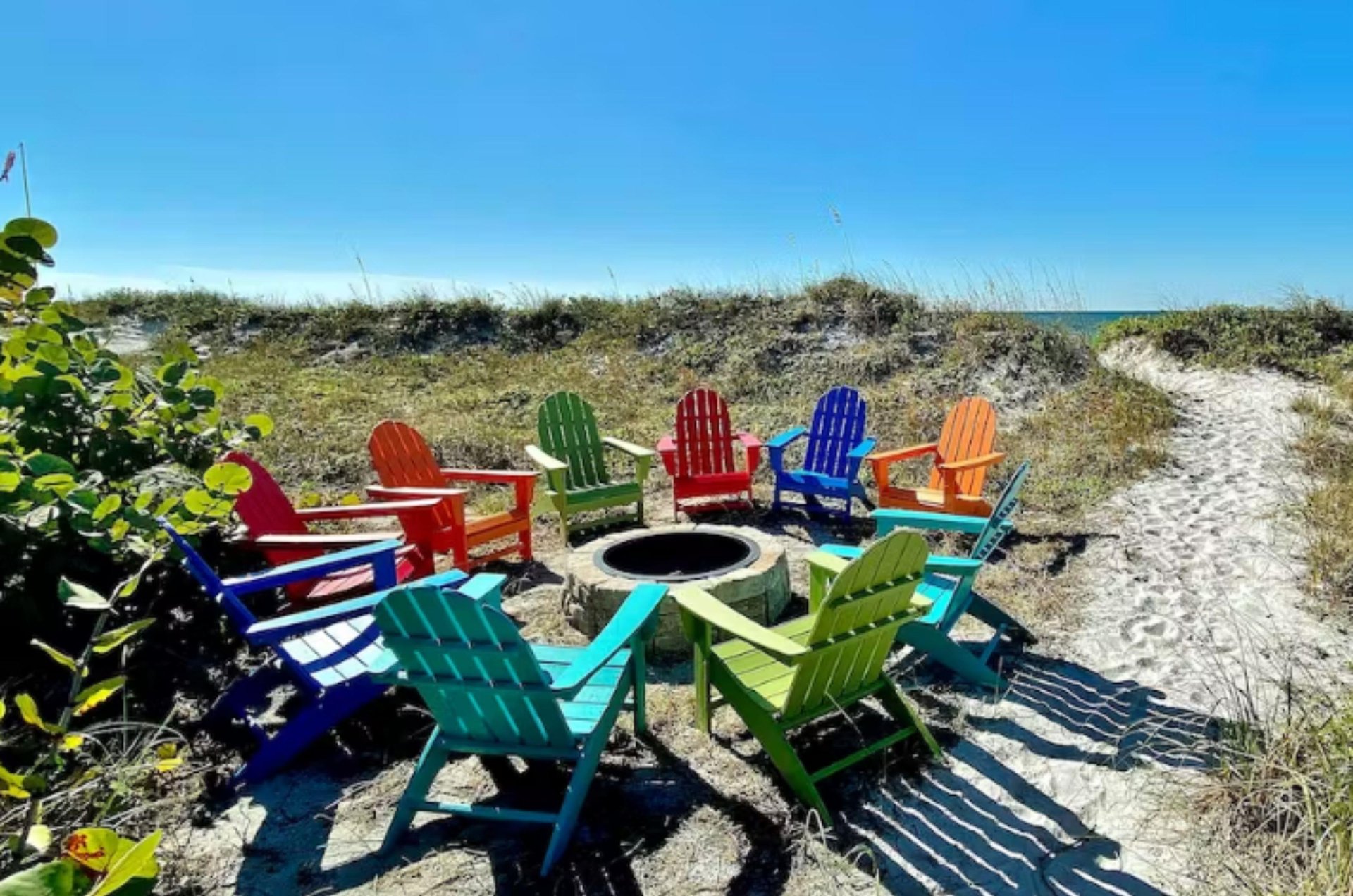 Brightly colored Adirondack chairs around a fire pit next to Clearwater Beach dunes.