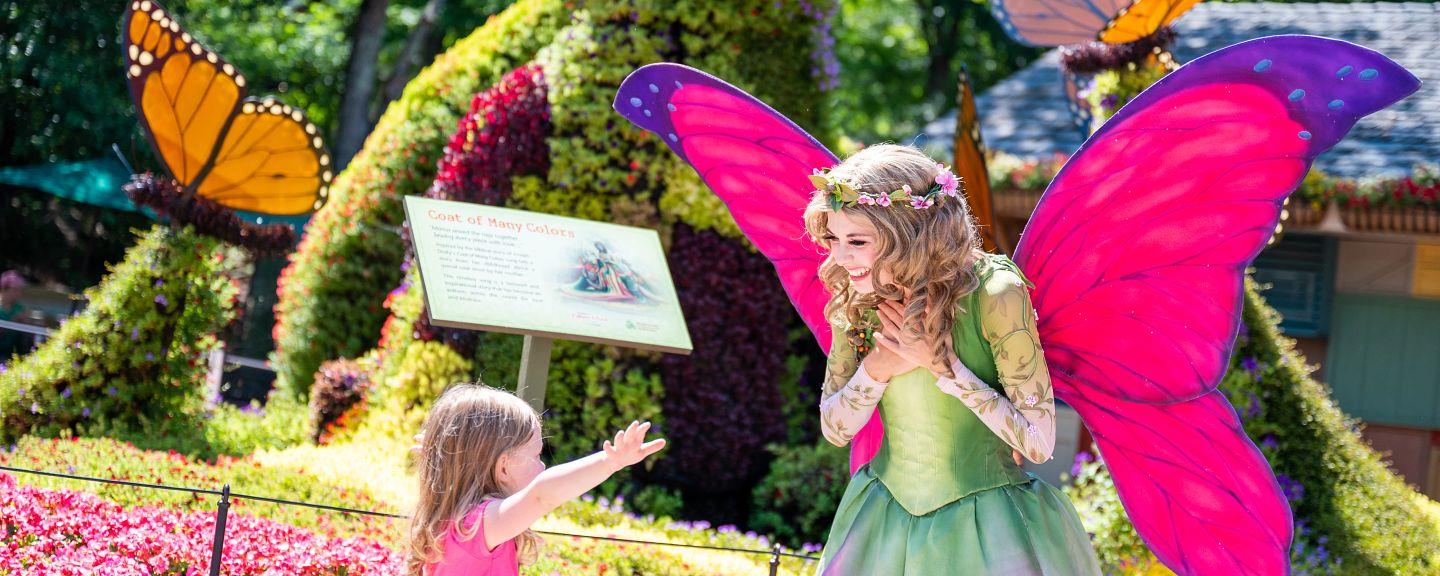 A costumed woman dressed as a fairy talks to a little girl