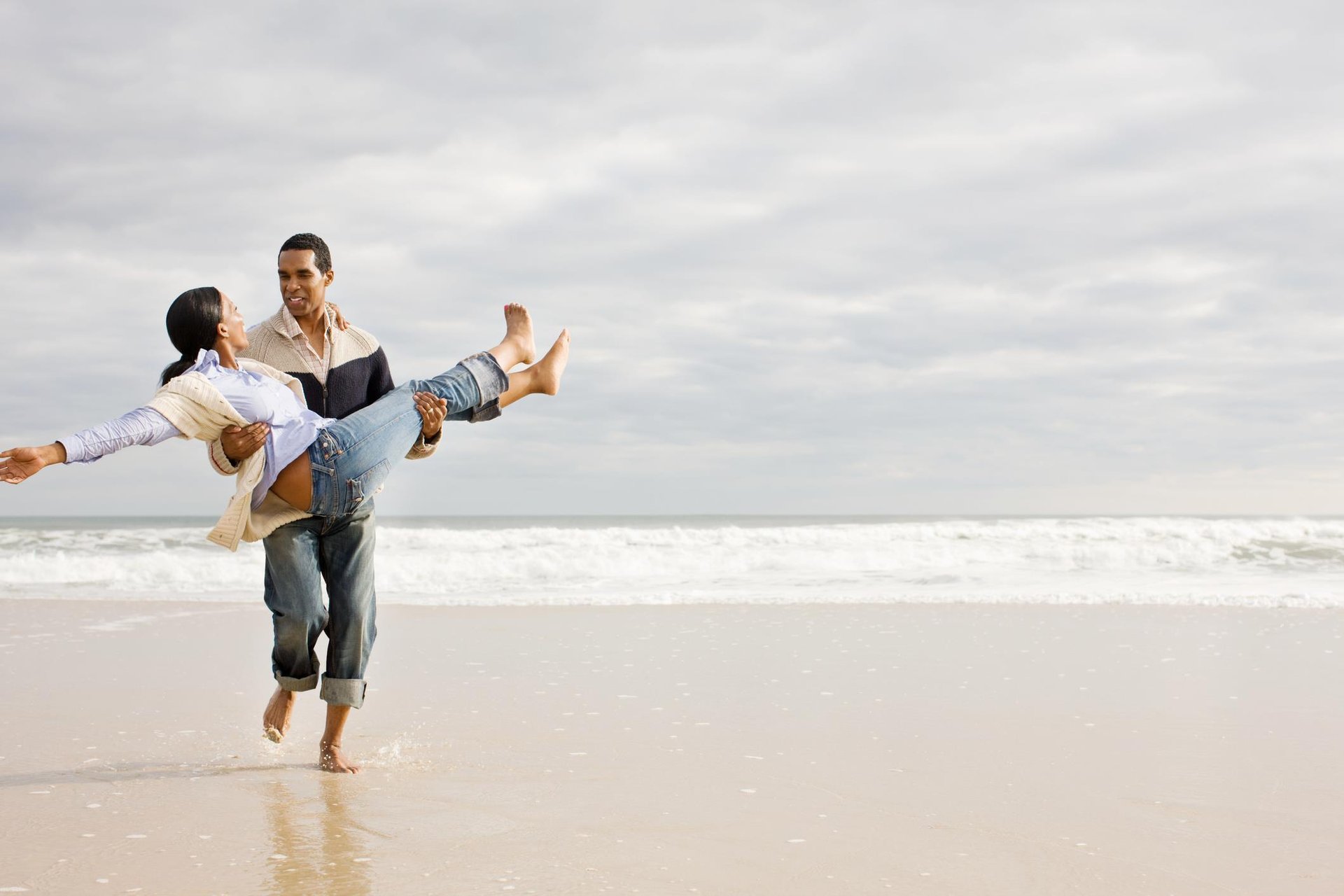 man carrying woman on beach in fall
