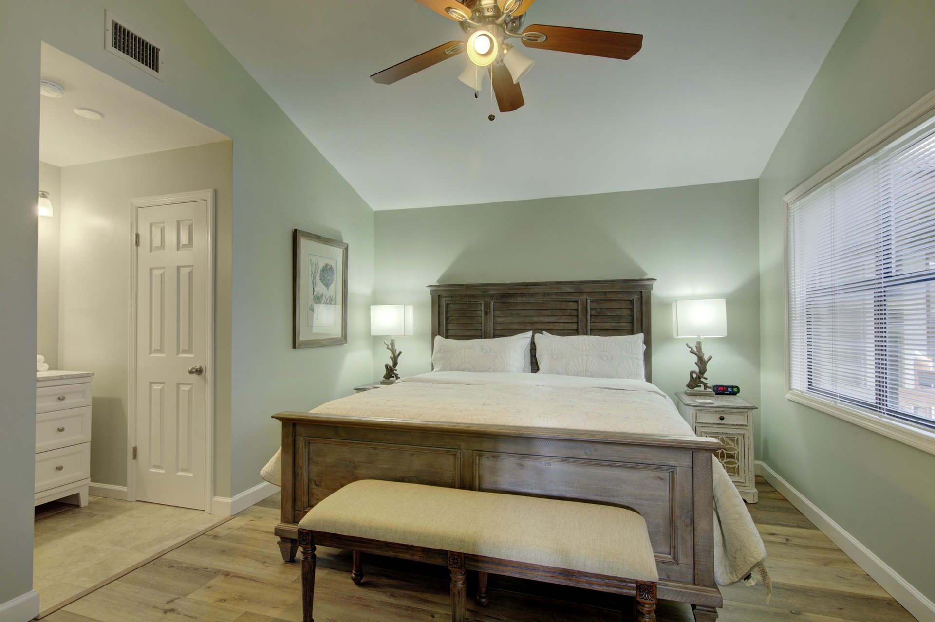 The serene king suite at 406 Harbour Oaks includes direct access to an en suite bathroom, plus soft lighting and windows on two sides for a calm, coastal feel.