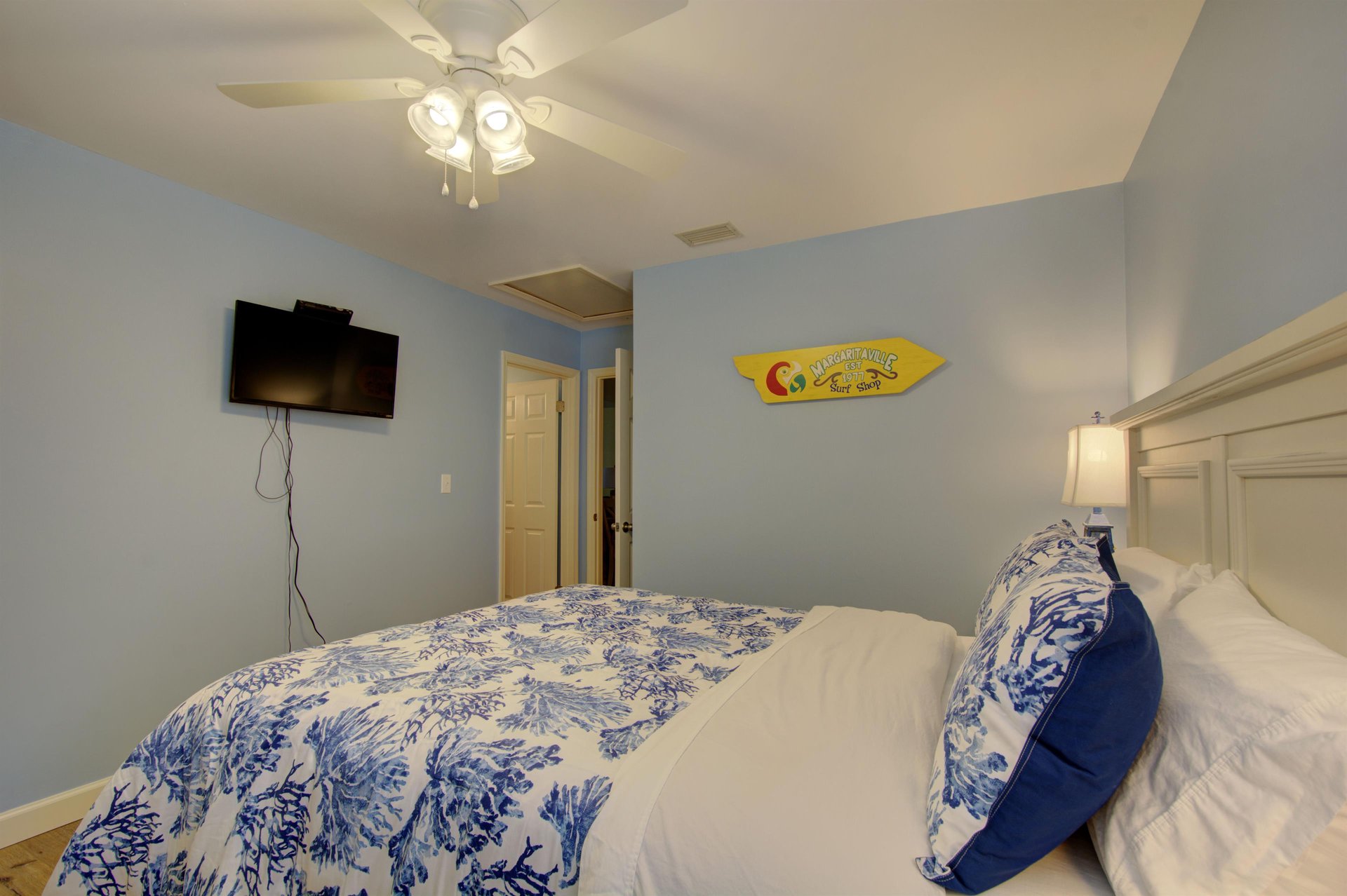 Guests can wind down with their favorite shows in this inviting queen bedroom, complete with wallmounted TV, ceiling fan, and a splash of playful coastal flair.