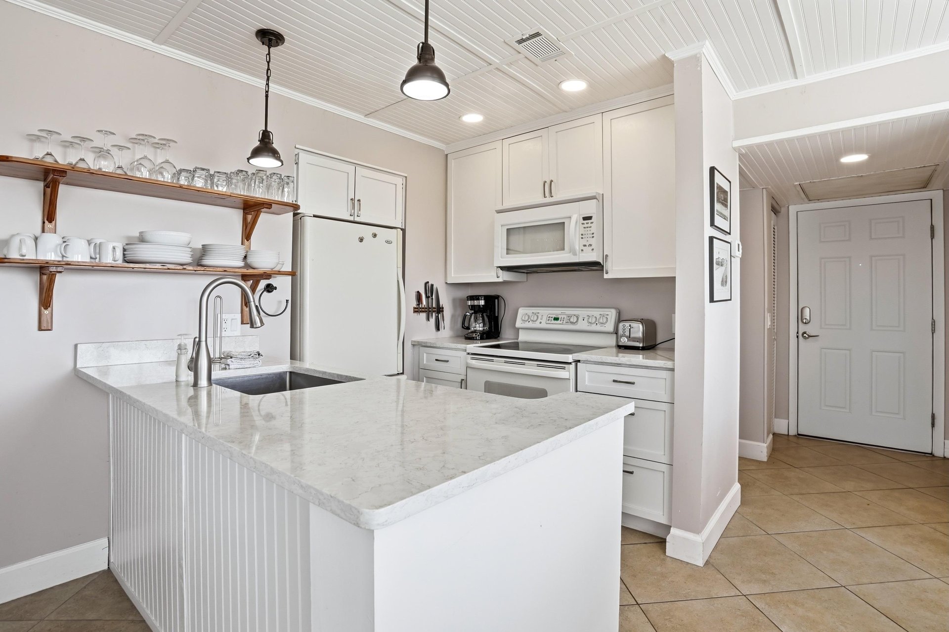 This coastal kitchen features open shelving and an easy layout, making it comfortable for quick meals and gathering between beach outings.