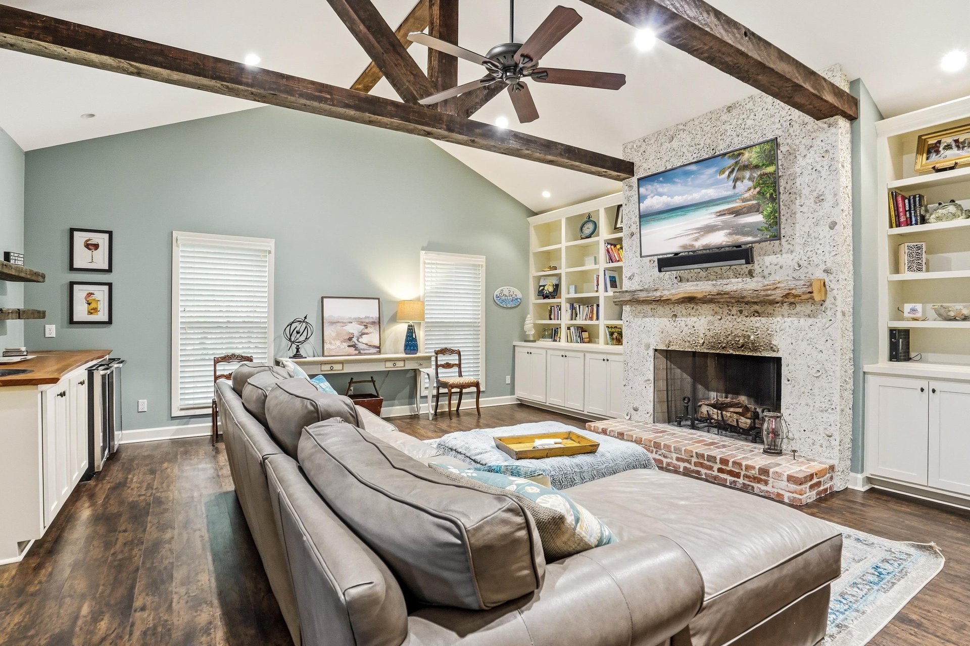 Exposed wood beam ceiling, stone fireplace, full builtin bookshelves flanking the TV, and a sectional sofa big enough for everyone — this is the room people come back for.