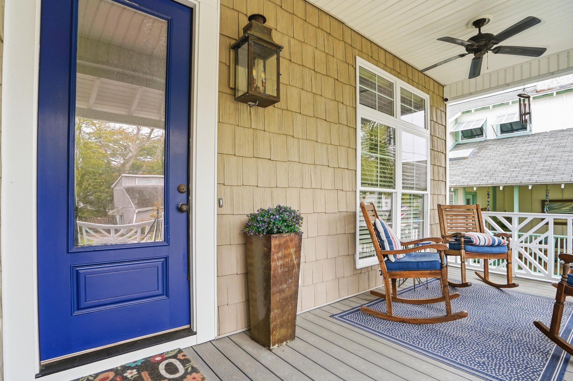 The covered front porch with rocking chairs, a ceiling fan, and a bold blue front door — the tone is set before you step inside.