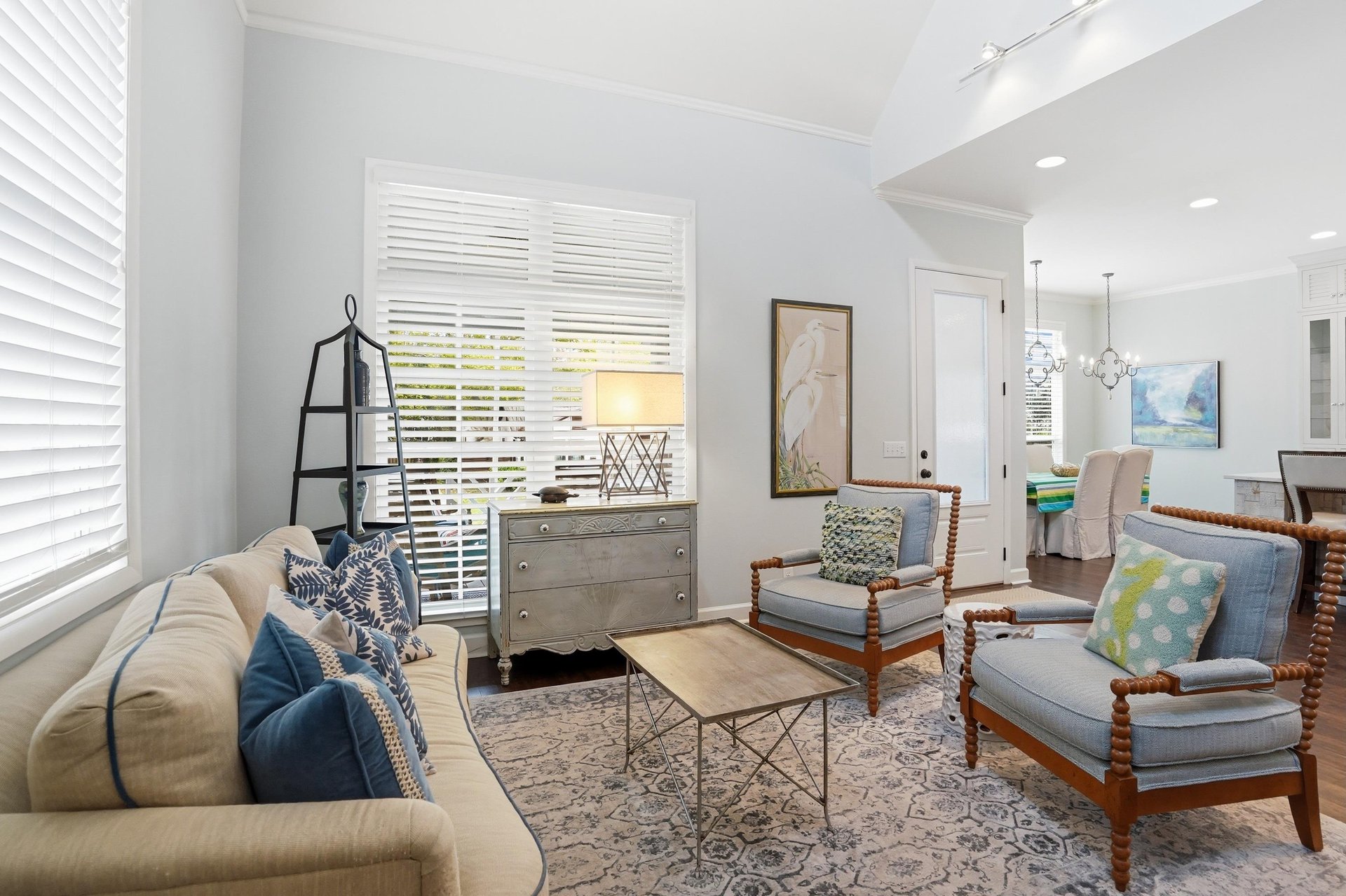 A comfortable living room anchored by a navy sofa, rattan accent chairs, and plantation shutters filtering the natural light.