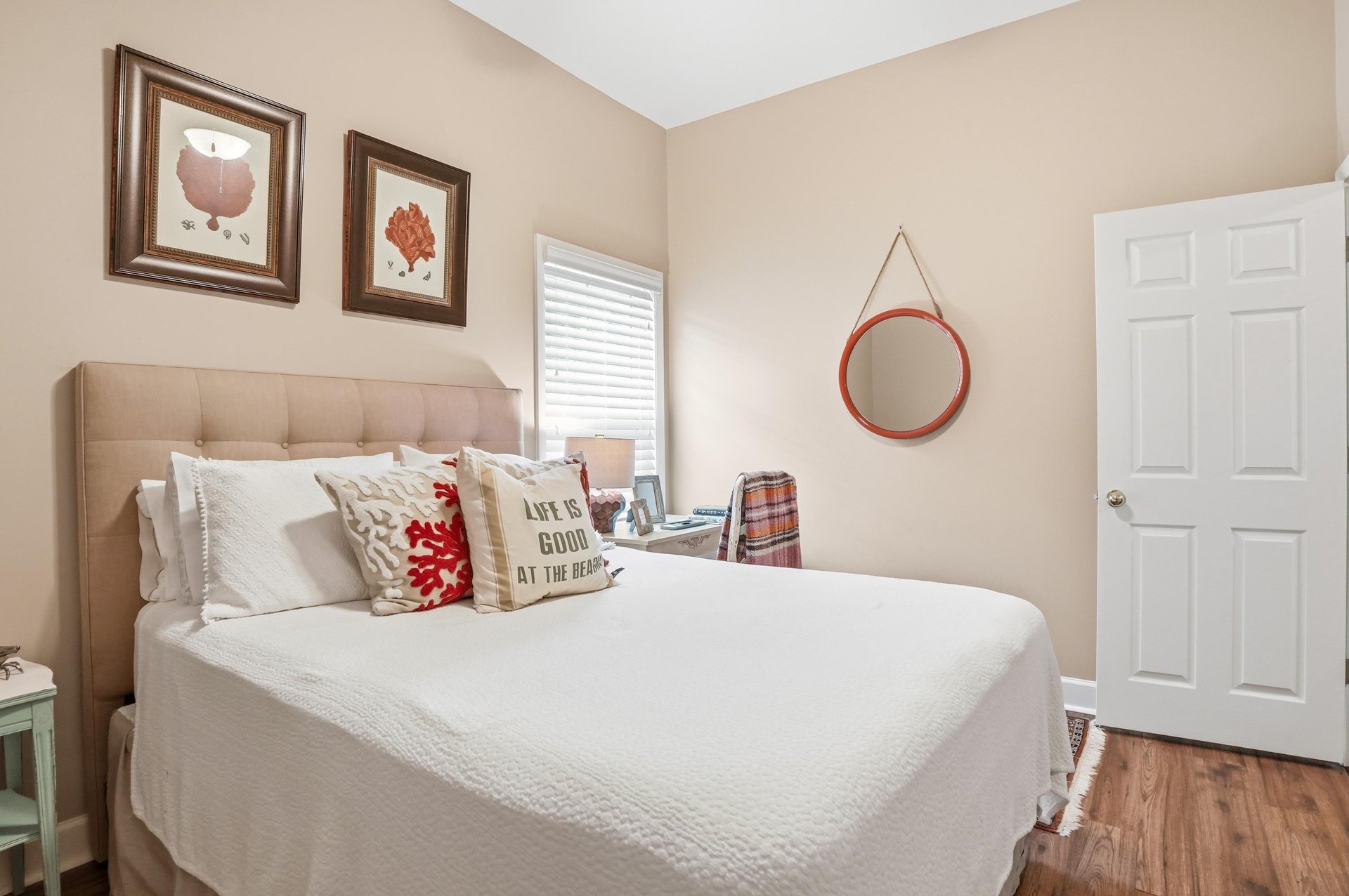 The full room from a wider angle — a round mirror, a bright white door, and warm natural tones throughout.