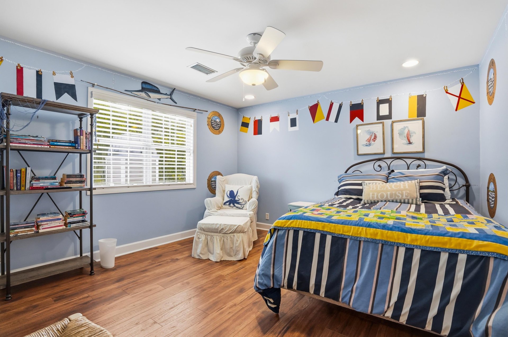 Navy accent wall, pennant flags, striped bedding, and a ladder bookshelf — the kids will claim this one on sight.