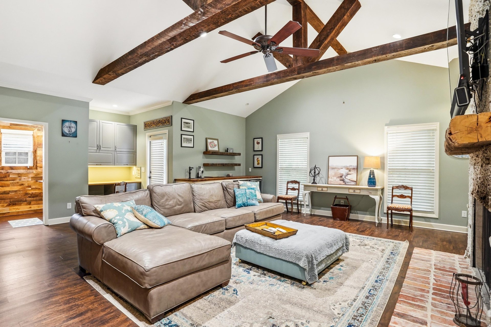 The den sectional from the opposite angle — ceiling beams and stone fireplace still commanding the backdrop.