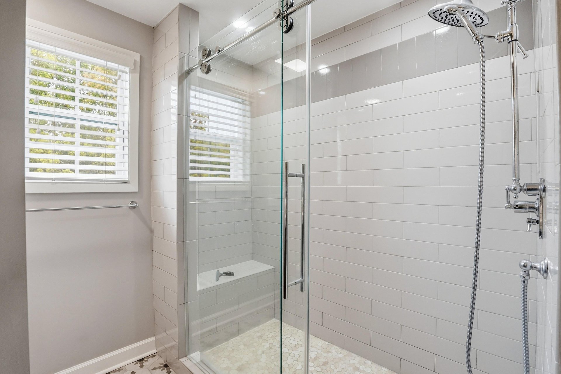 Walkin shower with glass enclosure, rainfall showerhead, subway tile walls, and a plantation shutter window — a proper shower.