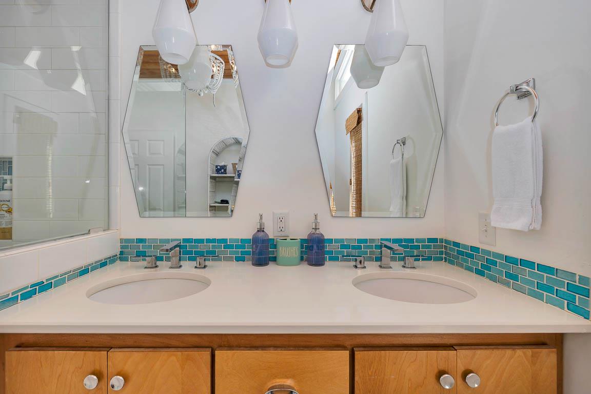Primary bathroom at 530 Delegal showing a dual vanity with two sinks, wood cabinetry, tiled backsplash, mirrors, and wallmounted lighting.
