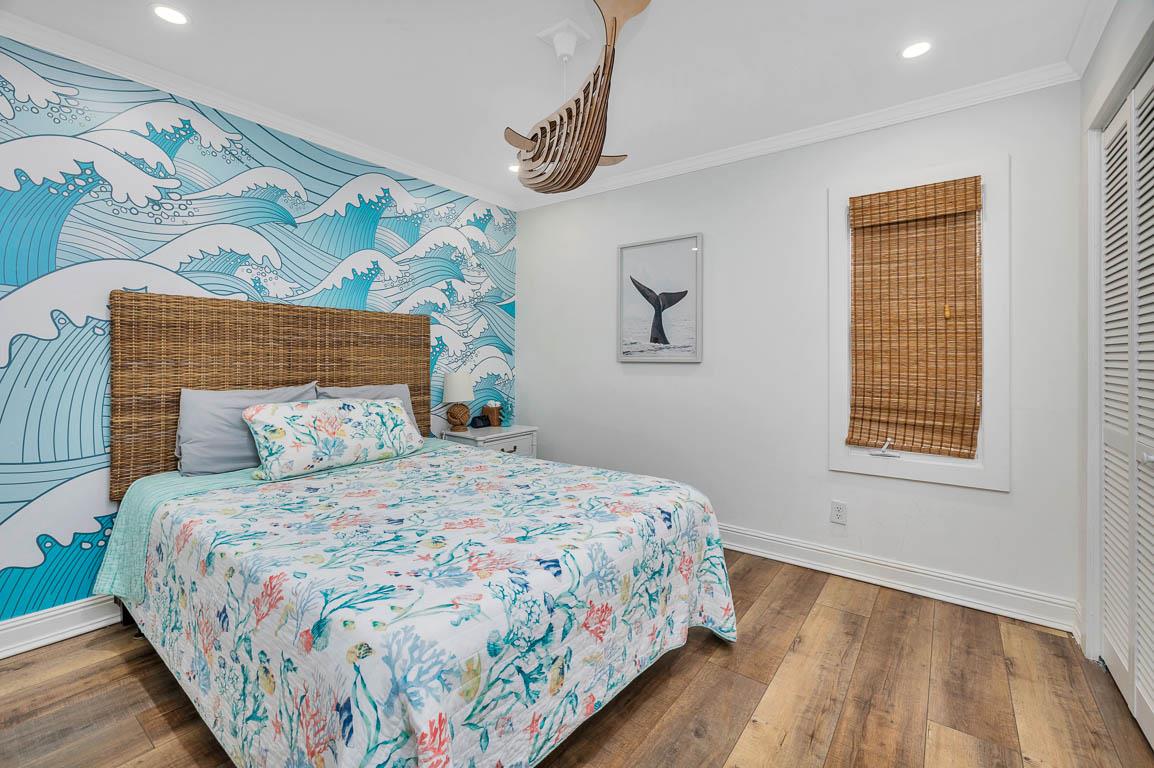 Guest bedroom in the main house at 530 Delegal showing a queen bed, wall art, wood flooring, window with shade, and a wooden whale light fixture.