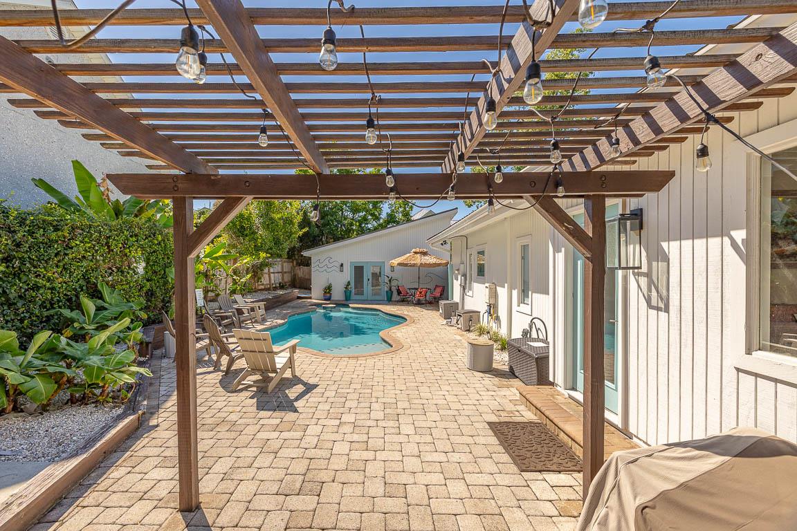 Pergolacovered walkway through the gated courtyard at 530 Delegal showing paver decking, lounge seating, and access between the guest house and heated pool.