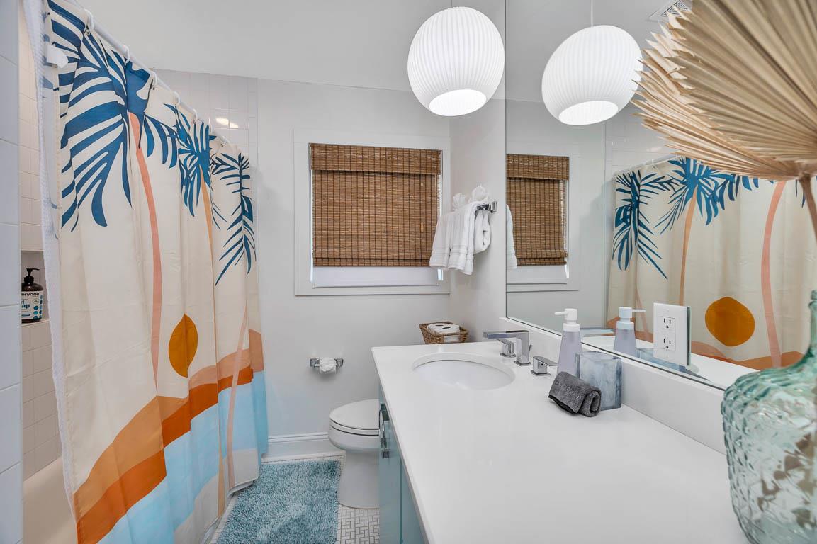 Hallway bathroom in the main house at 530 Delegal showing a tub and shower combination, single vanity with sink, mirror, lighting, and window with shade.