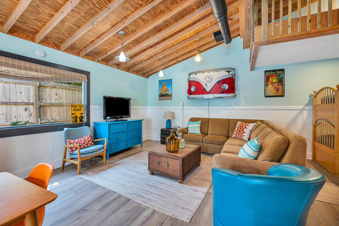 Alternate view of the guest house living area at 530 Delegal showing seating, television, exposed ceiling, loft railing above, and access to the sleeping area.