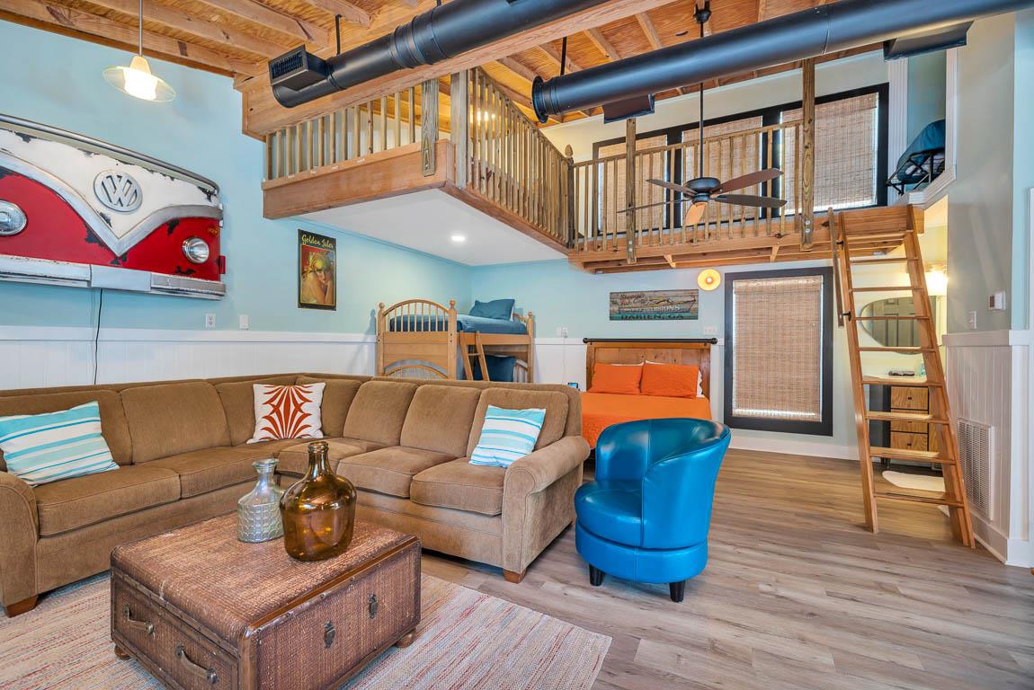 Interior of the guest house at 530 Delegal showing the living area, bed, bunk beds, ladder access to the loft, and open upperlevel railing.