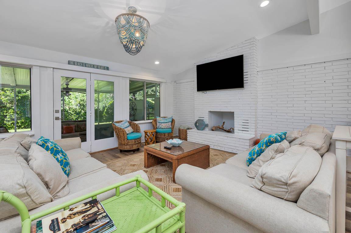 Additional view of the main house living room at 530 Delegal showing seating arranged around the fireplace and television, with glass doors leading to the screened porch.