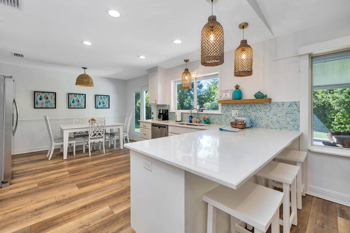 View of the main house kitchen at 530 Delegal showing island seating, countertop workspace, cabinetry, pendant lighting, and the dining area beyond.
