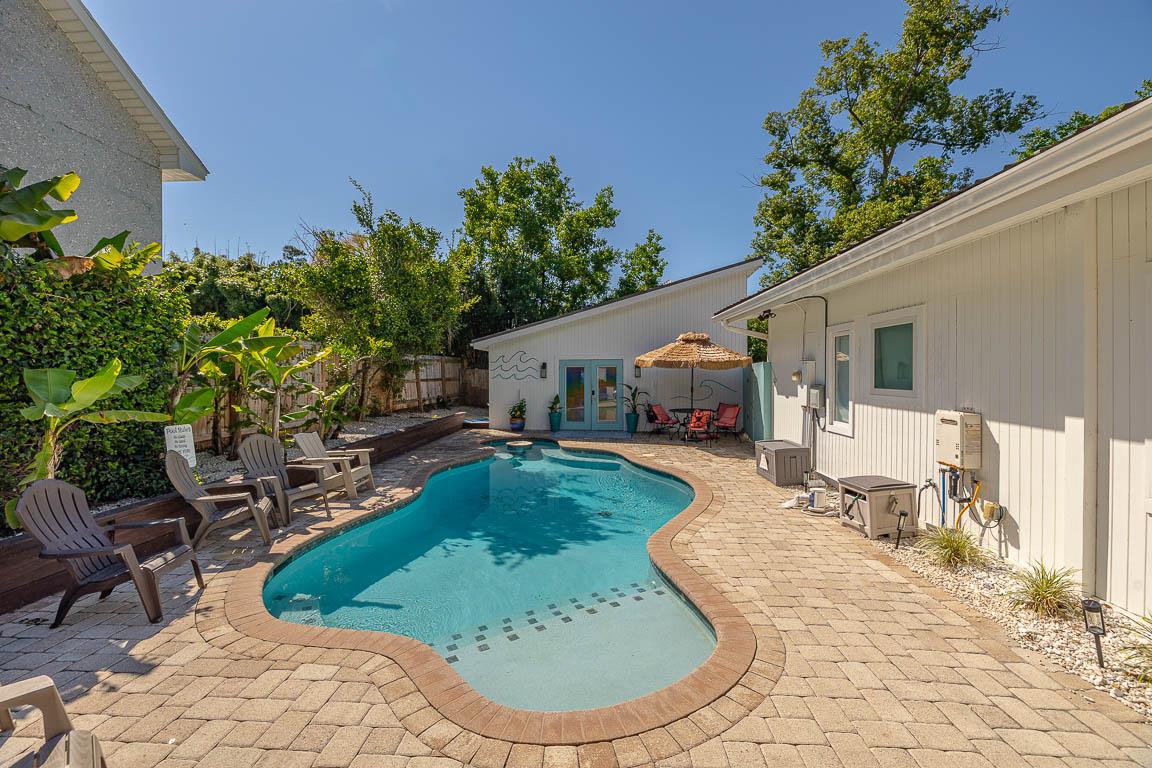 Groundlevel view of the heated pool at 530 Delegal showing the paver deck, lounge seating, and the pool running alongside the guest house within the gated courtyard.