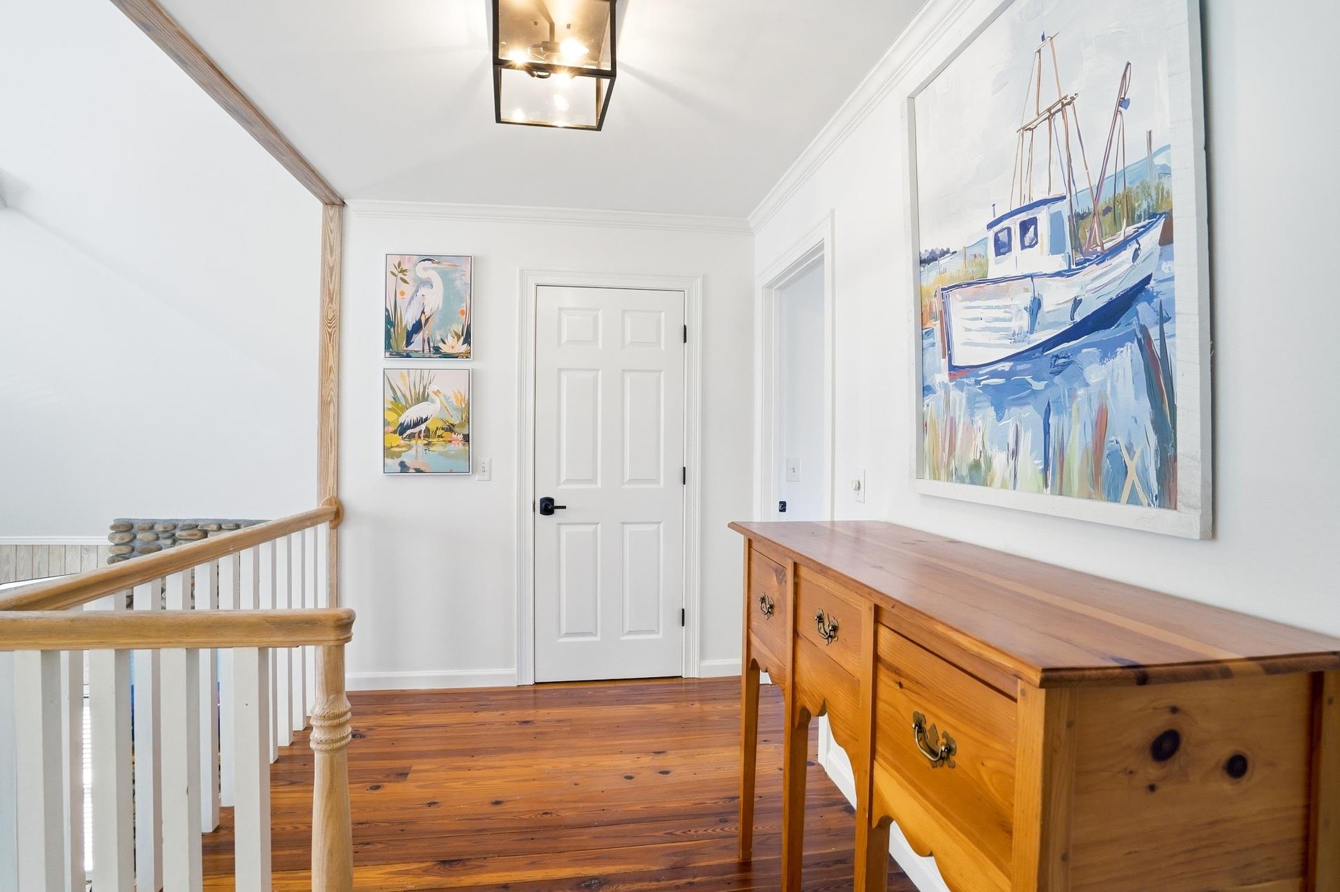 Upstairs landing connecting the upperlevel bedrooms, with hardwood floors and a railing overlooking the main living area.