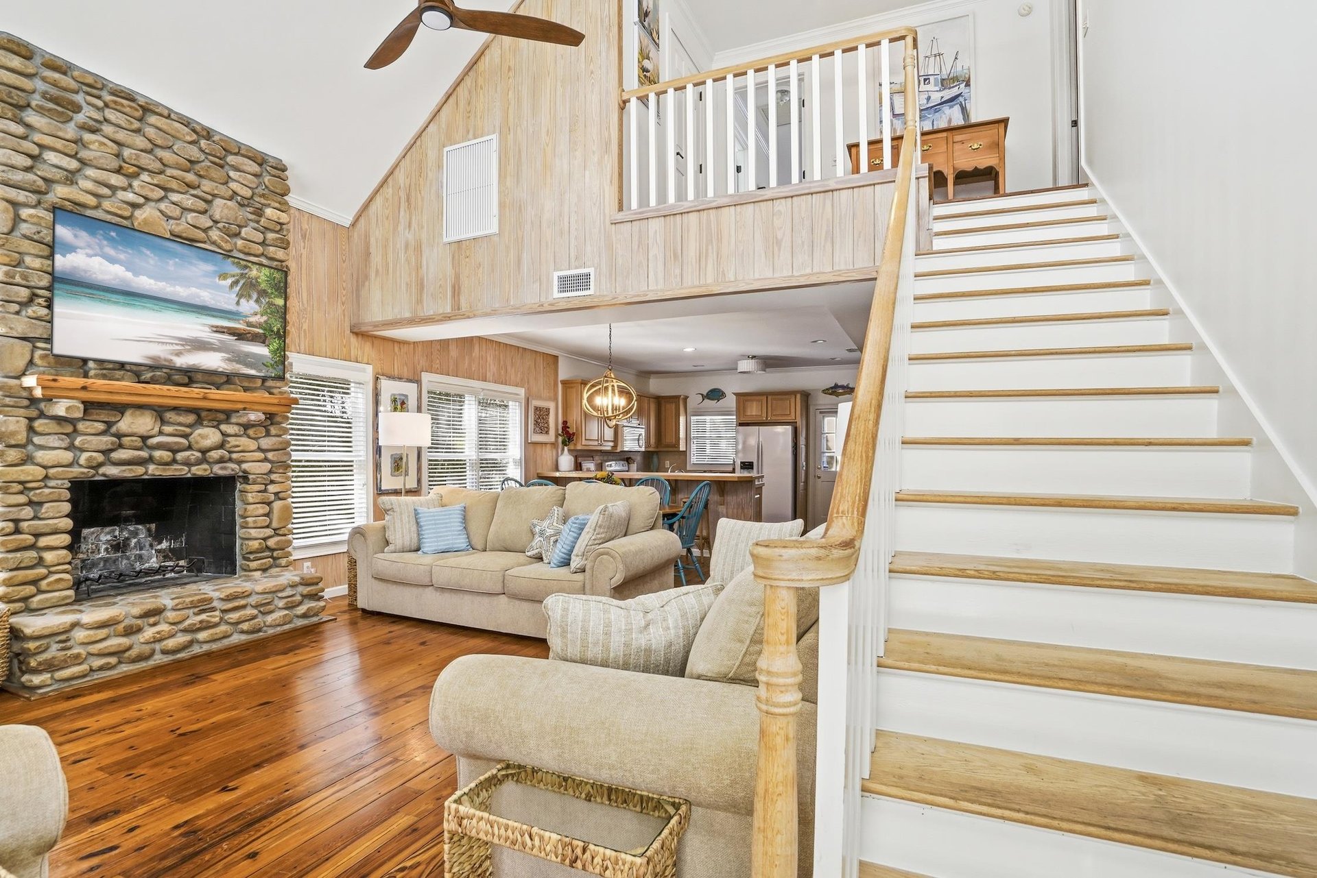Main living room view from the entry with hardwood floors, stone fireplace, and staircase to the upstairs bedrooms.