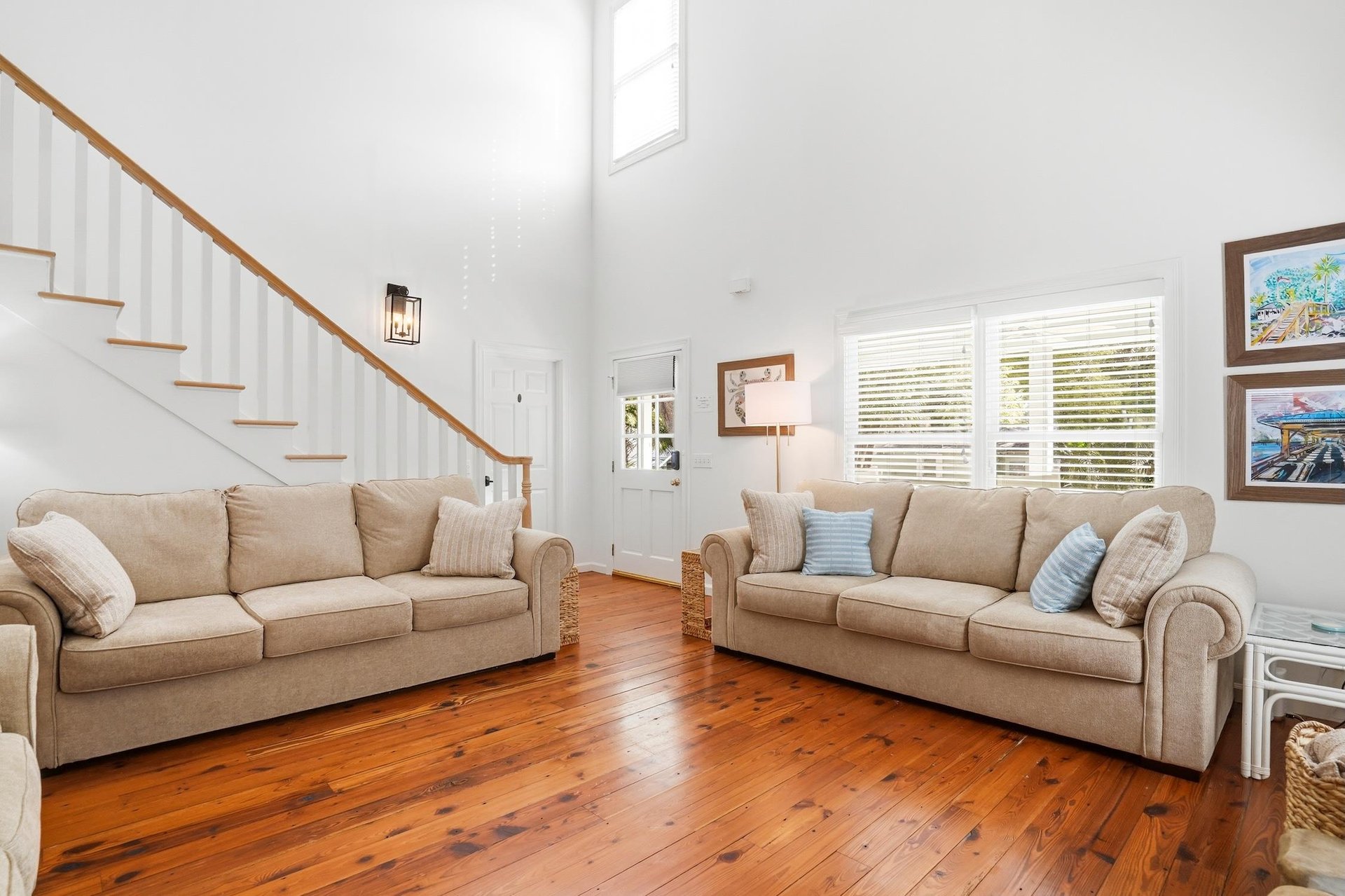 Alternate living room angle showing the seating area, staircase, tall ceiling, and natural light.