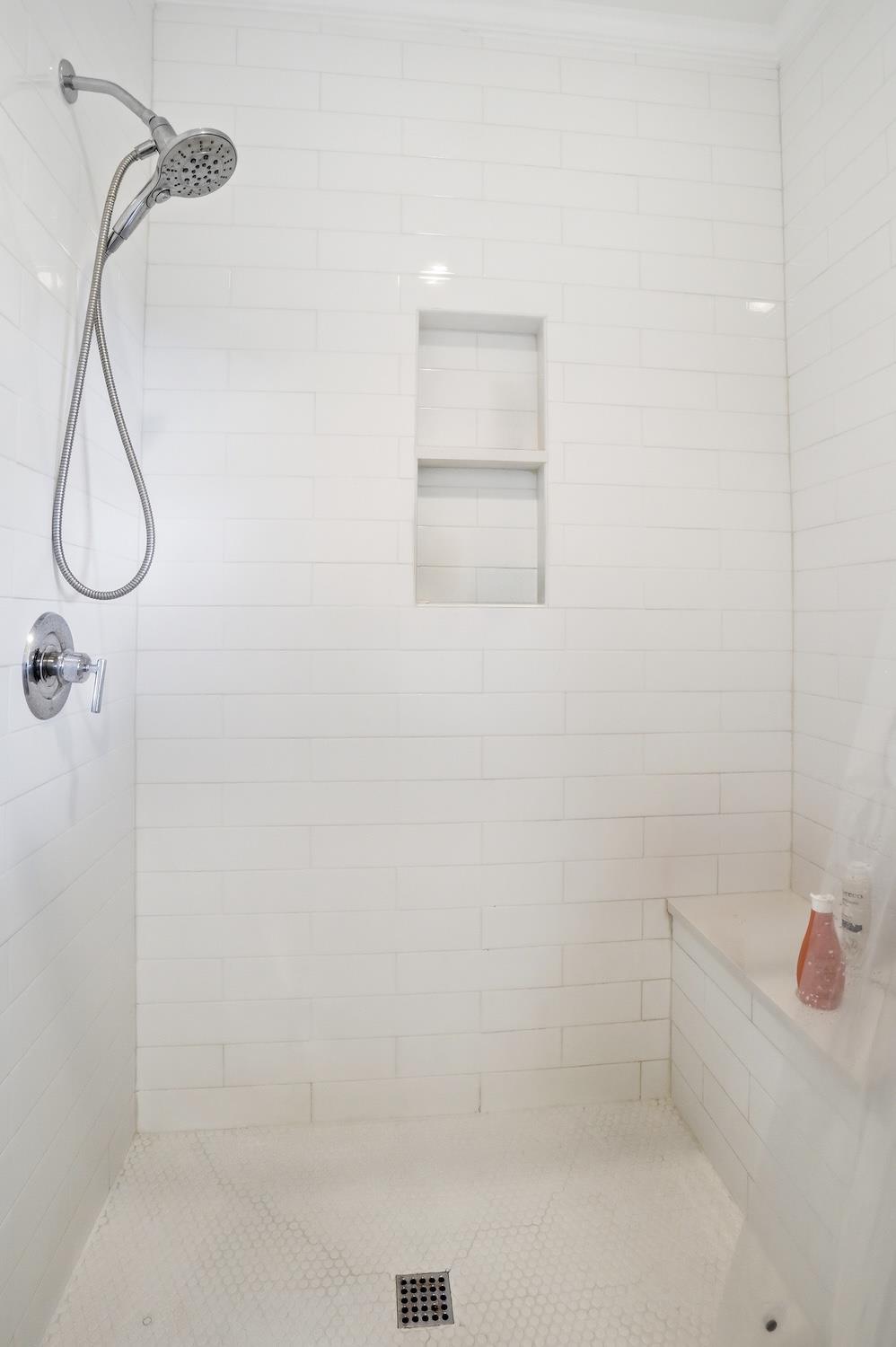 Walkin shower with white tile surround and builtin niche in the main floor primary ensuite bathroom.