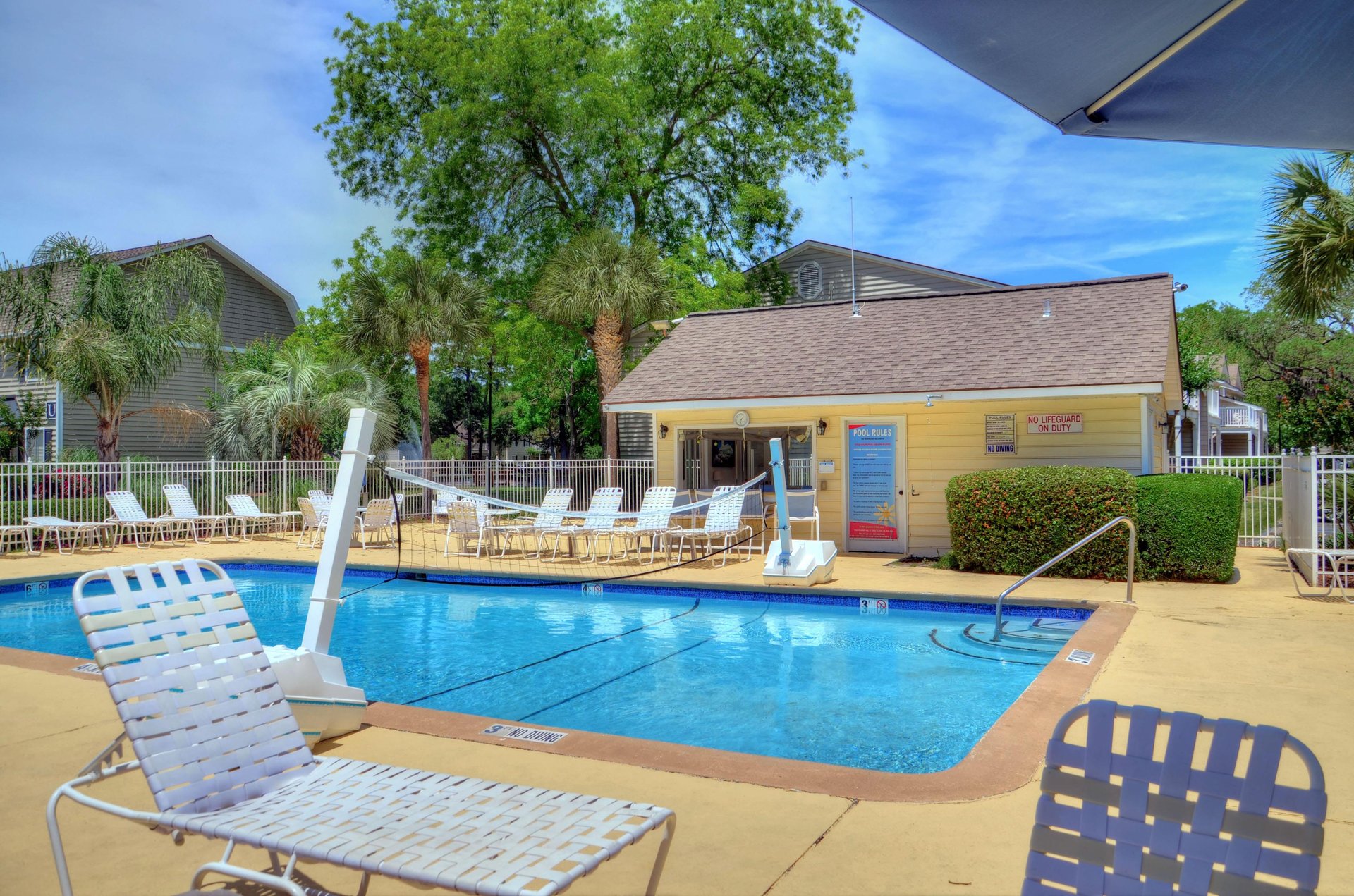 Seasonally heated pool with lounge chairs, palms, and clubhouse access nearby.
