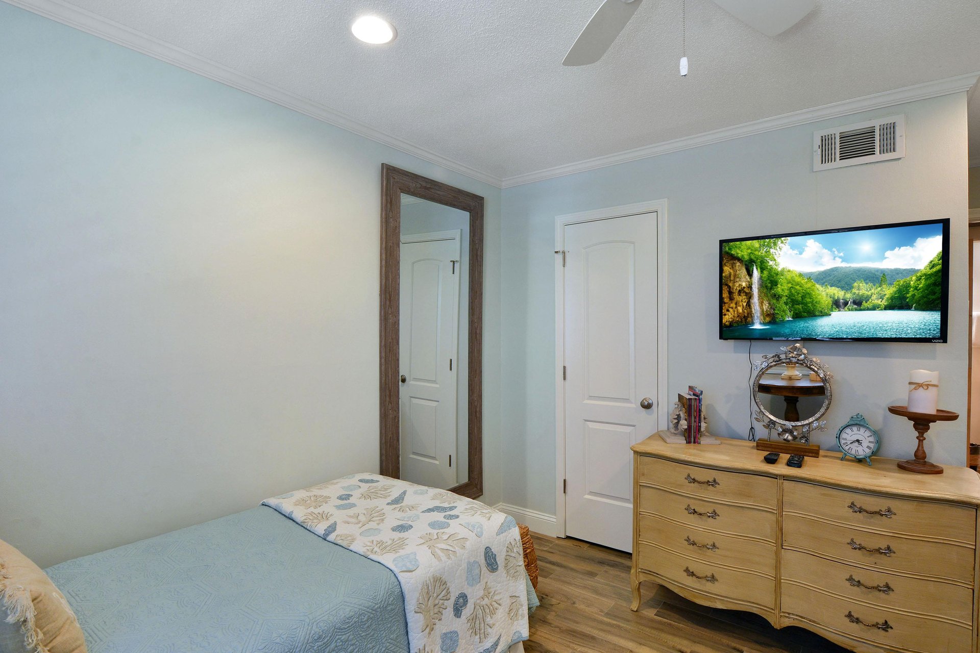 Guest bedroom angle with twin bed, dresser, mounted TV, and closet access.