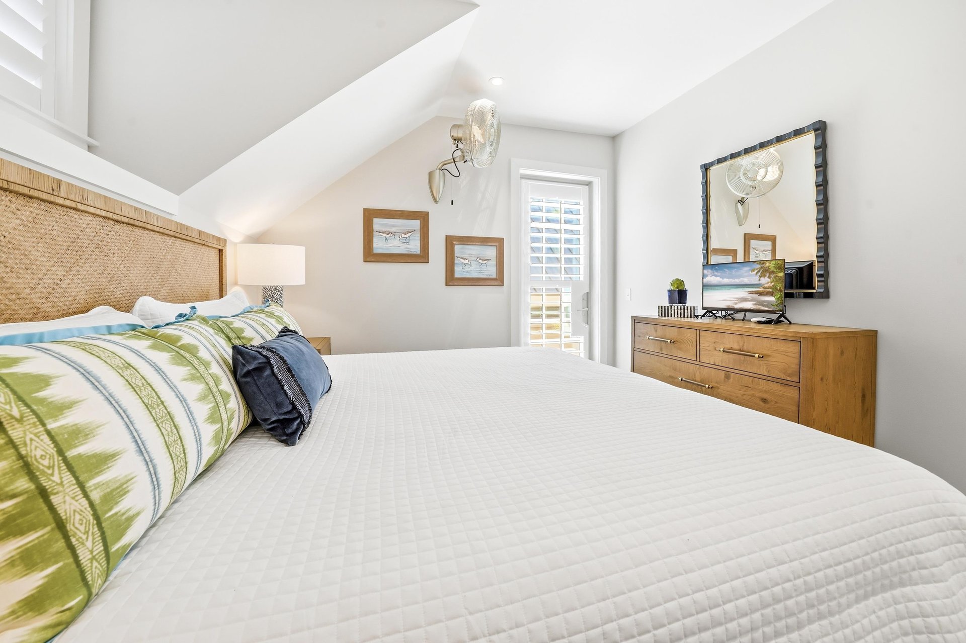 A wooden dresser and shuttered window sit across from the bed.