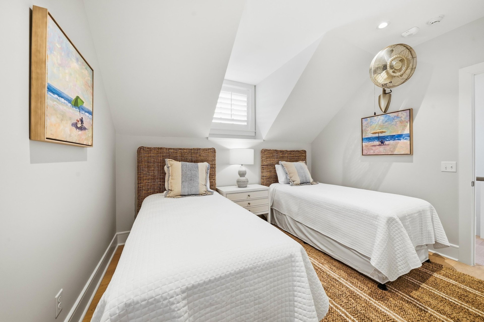 A shared bedside table sits between the twins, with a wallmounted fan above.