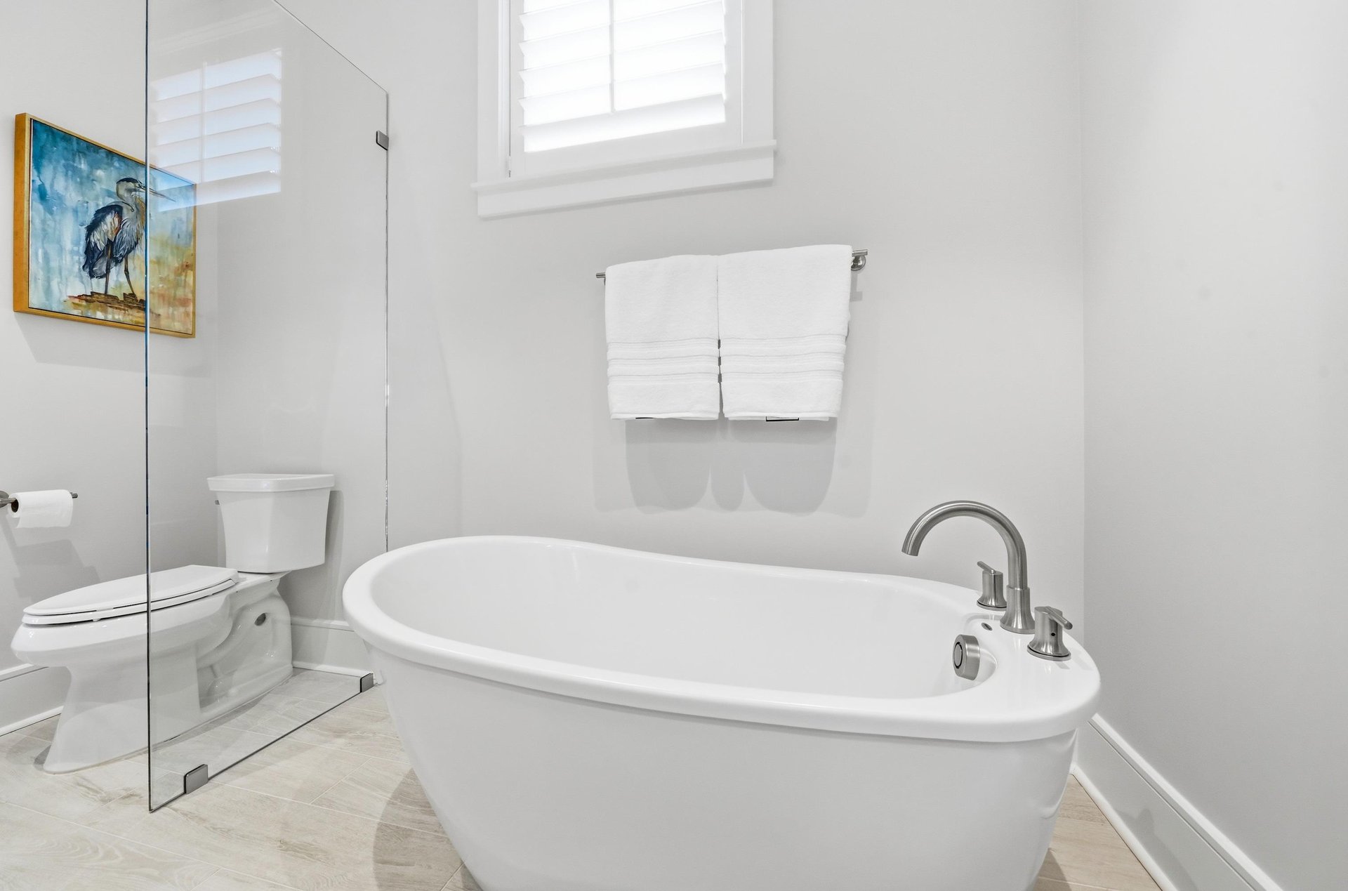 A tall shuttered window brings daylight beside the separate glass shower.