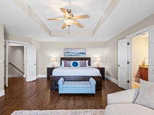 Relax in your spacious primary bedroom featuring a king bed, elegant tray ceiling, and comfortable seating area for the perfect retreat.