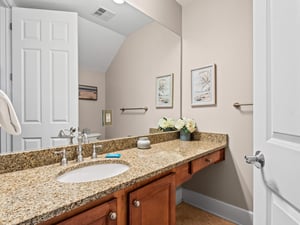 Step into your half bathroom featuring granite countertops, warm wood cabinetry, and thoughtful coastal artwork that creates a serene atmosphere for your daily routine.