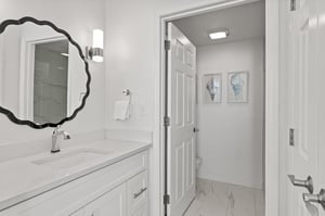 Step into your pristinely clean bathroom featuring elegant marble countertops, stylish scalloped mirror, and thoughtful touches that make your morning routine feel luxurious.