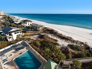 Stunning beachfront property aerial view showcasing pristine white sand beach, turquoise waters, and luxury vacation homes along the coastline.