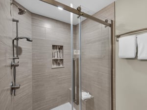 Step into your spacious glassenclosed shower with elegant woodgrain tiles and modern fixtures for your daily refresh.