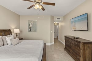 Unwind in your serene bedroom with plush bedding, coastal artwork, and a gentle ceiling fan keeping you cool during peaceful nights.