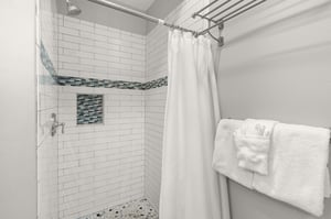 Step into the pristine tiled shower featuring elegant white subway tiles and blue mosaic accents with fluffy towels awaiting.