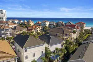 Coastal community overlooking pristine turquoise waters and white sand beaches, surrounded by tropical palm trees and residential buildings.