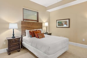 Sink into crisp white linens and colorful accent pillows in your peaceful bedroom retreat with warm lighting and coastal artwork.