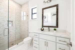 Step into your pristine bathroom where white marble meets exposed brick. The spacious shower and elegant vanity create a perfect morning retreat.