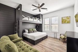 Your stylish bedroom features custom bunk beds, plush green seating, and modern comfort with a ceiling fan to keep you cool.